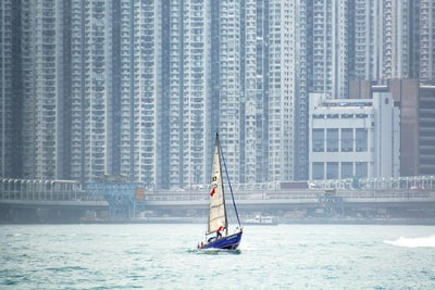 During the day, white and blue boat sailing in high-rise building near the sea

